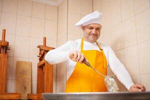 uomo fa formaggio, bolle latte nel cisterna, il riscaldamento, temperatura. latte pieghevole processi, casa produzione, attività commerciale, individuale imprenditore. ritratto. foto