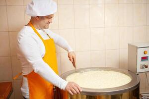 uomo fa formaggio, bolle latte nel cisterna, il riscaldamento, temperatura. latte pieghevole processi, casa produzione, attività commerciale, individuale imprenditore. cucinare. foto