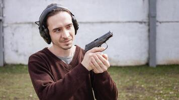 un' uomo è mirando per un' pistola. un' uomo indossare protettivo cuffia. all'aperto pneumatico tiro gamma. passatempo. arma contro il bianca parete foto