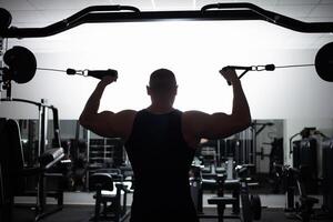 ritratto di un atleta, un' gli sport uomo allenatore fa un esercizio su simulatore nel il palestra. salutare attivo stile di vita, scuote muscoli. foto