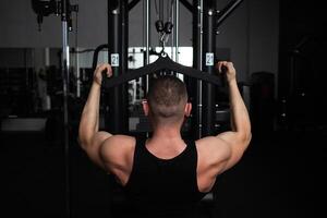 ritratto di un' bello maschio allenatore nel palestra. il atleta fa un esercizio su il simulatore nel il palestra. costruisce muscolo, giochi gli sport, un' salutare stile di vita. posteriore Visualizza foto