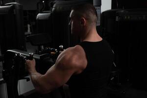 ritratto di un' bello maschio allenatore nel palestra. il atleta fa un esercizio su il simulatore nel il palestra. costruisce muscolo, giochi gli sport, un' salutare stile di vita. si siede foto