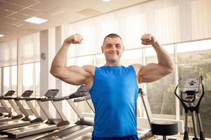 un' giovane bello allenatore con un' muscolare corpo pose nel palestra. bodybuilder, gli sport fisico terapia, peso perdita. sport è un' freddo, salutare attivo stile di vita. interno concetto. grande muscoli, sorrisi foto