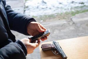 un' uomo addebiti un' pistola con proiettili. Pericolo, omicidio, armi da fuoco, tiro gamma, gli sport intrattenimento. foto