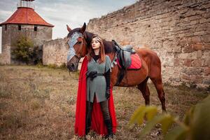 bellissimo Principessa con rosso capo sta Il prossimo per il cavallo contro il fondale di un' Torre e un' pietra parete foto