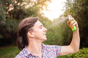 giovane uomo spruzzatura zanzara insetto repellente nel il foresta, protezione. un' uomo spray zanzara spray su il suo viso. foto