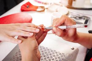 il manicure detiene mani di il cliente nel bellezza salone su del desktop per manicure con chiodo lucidi, tovaglioli, creme e illuminazione strumenti foto