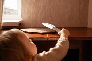 il bambino tira un' coltello a partire dal il tavolo. il bambino può tagliare, figli di casa pericoli. un' poco un anno ragazza con un' coltello. foto