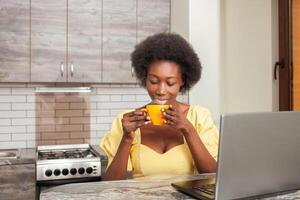 bellissimo africano americano donna bevande tè nel cucina. godendo bere, caldo caffè nel mattina, prima colazione. caricare di energia e vivacità per totale giorno. foto