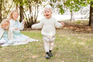 contento poco ragazza nel bianca collant e fasce su un' picnic con sua sorelle. il bambino è apprendimento per camminare. foto