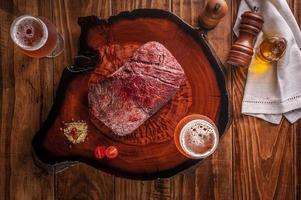 bistecca di Denver alla griglia con due bicchieri di birra sul tagliere di legno. manzo di carne di marmo - vista dall'alto. foto