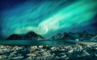 settentrionale luci raggiante al di sopra di nevoso montagna gamma su costa a skagsanden spiaggia, lofoten isole foto