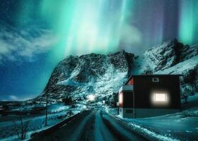 scenario di aurora Borealis o settentrionale luci danza al di sopra di nevoso montagna nel scandinavo villaggio su inverno a lofoten isole foto