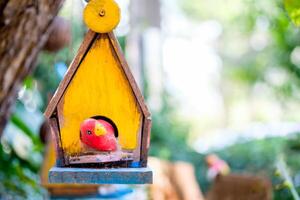 giallo di legno casa nido uccello con rosso uccello fatto a mano sospeso su sfondo foto