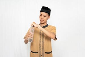 asiatico musulmano uomo indossare musulmano Abiti trasporto minerale acqua nel un' bottiglia mentre apertura il coperchio. isolato bianca sfondo. foto