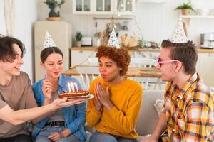 rendere un' desiderio. donna indossare festa berretto soffiaggio su ardente candele su compleanno torta. contento compleanno festa. gruppo di amici auguri ragazza contento compleanno. persone festeggiare compleanno con festa a casa foto