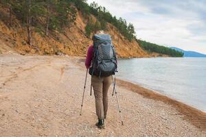 escursioni a piedi turismo avventura. irriconoscibile escursionista ragazza turista con zaino a piedi vicino lago. zaino in spalla donna godendo bellissimo spiaggia Visualizza. indietro Visualizza donna godere escursione il trekking turismo attivo vacanza foto