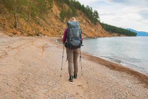 escursioni a piedi turismo avventura. irriconoscibile escursionista ragazza turista con zaino a piedi vicino lago. zaino in spalla donna godendo bellissimo spiaggia Visualizza. indietro Visualizza donna godere escursione il trekking turismo attivo vacanza foto