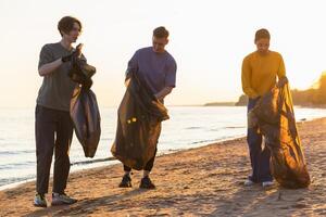 terra giorno. volontari attivisti squadra raccoglie spazzatura pulizia di spiaggia costiero zona. donna mans con spazzatura nel spazzatura Borsa su oceano costa. ambientale conservazione costiero zona pulizia foto