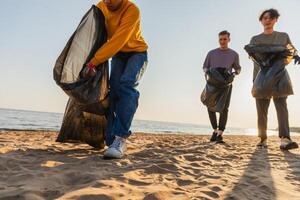 terra giorno. volontari attivisti squadra raccoglie spazzatura pulizia di spiaggia costiero zona. donna mans mette plastica spazzatura nel spazzatura Borsa su oceano costa. ambientale conservazione costiero zona pulizia foto