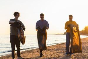 terra giorno. volontari attivisti squadra raccoglie spazzatura pulizia di spiaggia costiero zona. donna mans con spazzatura nel spazzatura Borsa su oceano costa. ambientale conservazione costiero zona pulizia foto