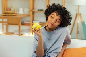 contento bella ragazza pungente verde Mela a casa. bellissimo africano americano giovane donna mangiare fresco frutta e sorridente. salutare cibo vegano vegetariano dieta concetto. salutare merenda pulito cibo foto