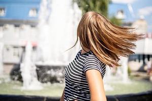 bella donna in abiti casual che si diverte a girarsi sullo sfondo di una fontana urbana in una giornata di sole foto