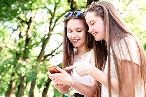 due donne felici che parlano nel parco usando il cellulare foto
