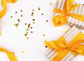 regali di natale avvolti con carta dorata e bianca, coriandoli e un nastro dorato vista dall'alto piatto foto