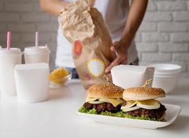 donna in abiti domestici disimballaggio cibo consegna a domicilio wit hamburger, scatole di noodle e bevande