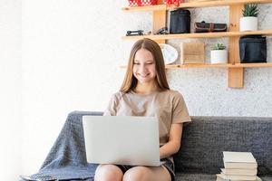 ragazza sorridente dell'adolescente che studia usando il suo computer portatile a casa foto