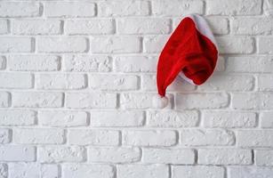 cappello rosso di babbo natale appeso a un muro di mattoni bianchi
