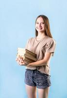 ragazza adolescente felice che tiene una pila di libri isolati su sfondo blu foto