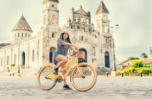 contento ragazza nel cappello equitazione un' bicicletta a tramonto. turismo e viaggio concetto. stile di vita di un' contento ragazza nel cappello su bicicletta su il strada. granada, Nicaragua foto