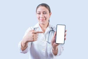 femmina medico mostrando e puntamento un annuncio pubblicitario su il smartphone schermo isolato. sorridente femmina medico puntamento un App su il Telefono schermo foto