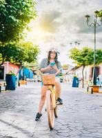 contento turista ragazza su bicicletta utilizzando cellula Telefono su il strada. bellissimo ragazza nel cappello su bicicletta con cellula Telefono su il strada di la calzada, granada, Nicaragua foto