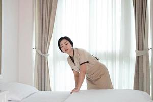 giovane e bella cameriera asiatica che sistema la coperta sul letto nella camera d'albergo foto