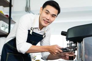 giovane uomo asiatico che usa la macchina per il caffè per preparare un espresso caldo. barista e caffè concetto di caffè foto