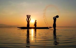 sagoma di pescatore e suo figlio in piedi nel lago vicino alla barca e usando un barattolo per spruzzare acqua foto