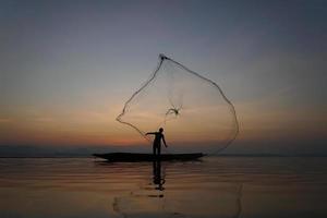pescatore che lancia la rete da pesca per catturare il pesce nel lago al mattino