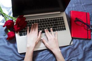 le mani femminili lavorano dietro un computer portatile a casa, un taccuino rosso e un mazzo di fiori su uno sfondo foto