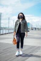 giocando ukulele di giovane bellissimo asiatico donna indossare giacca e nero jeans in posa all'aperto foto