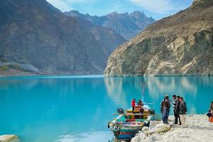 Gilgit baltistan, pakistan, 2017 - persone che noleggiano una barca colorata sul lago di attabad, con vista sulle montagne della catena del karakoram e sull'acqua turchese. gojal hunza. foto