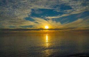 issykkul lago a tramonto, dove il di sole d'oro splendore incontra wispy nuvole e tranquillo acque, la creazione di un' riflessivo simmetria sotto il vasto mattina cielo, sereno nel suo naturale splendore. foto