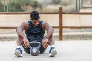atletico nero uomo riposo su gli sport terra con kettlebell foto