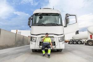 positivo maschio autista seduta su cofano di camion mentre parlando su smartphone foto