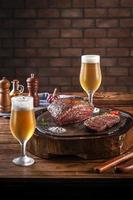 bistecca di scamone con cappuccio alla griglia su tagliere di legno con due bicchieri di birra tulipa freddi e sudati. tavolo in legno e muro di mattoni sfondo - picanha brasiliana. foto