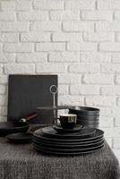 pila di piatti in ceramica nera e stoviglie sul tavolo su sfondo bianco muro di mattoni