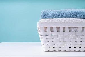 pila di asciugamani puliti in un cesto della biancheria bianco su sfondo blu foto