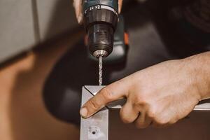 maschio meccanico lavori nel laboratorio con elettrico trapano. lavoratore trapani buco nel metallo. stile di vita, professionale attività. mani hold riparazione attrezzo. foto